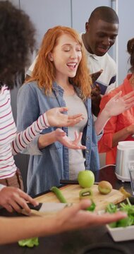 Vertical video of happy group of diverse friends preparing healthy drink in kitchen together