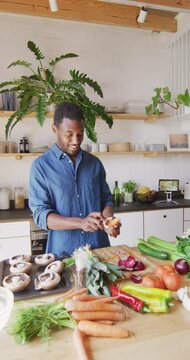 Vertical video of happy african american man standing in kitchen and cooking dinner