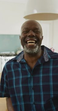 Vertical video portrait of happy senior african american man laughing to camera in kitchen
