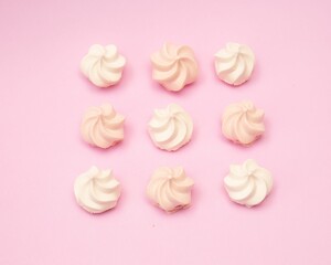Top view of nine white and pink mini meringue swirls on pink background