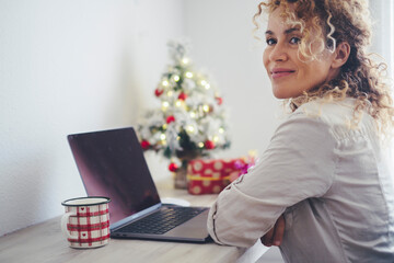 Side portrait view of attractive young adult woman smiling and thinking with laptop in front and...