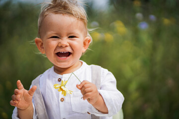 
one year old happy blond german baby boy in white shirt playing outside in the garden with a yellow flower to send love or congratulate for birthday
