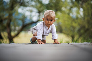 happy one year old baby boy sitting or crawling in chic festive summer clothes outdoor on the floor...