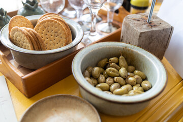 Green olives in a ceramic bowl, salted crackers, wine glasses on a table for guests