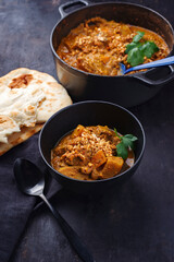 Traditional Indian vegetarian Madras curry stew with sweet potatoes, roasted cashew nuts and garlic chapati bread served as close-up in a design bowl