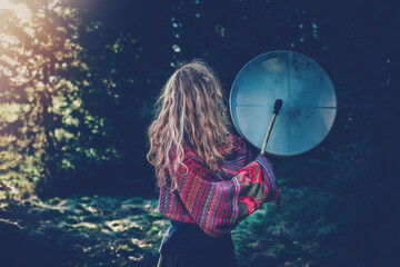 Beautiful shamanic girl playing on shaman frame drum in the nature.Shot from the back.