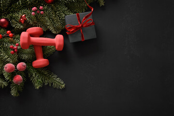 Christmas composition with gift, two red sports dumbbells, evergreen branches on black background....