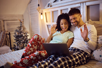 Happy couple greeting someone during video call over laptop on Christmas. - obrazy, fototapety, plakaty