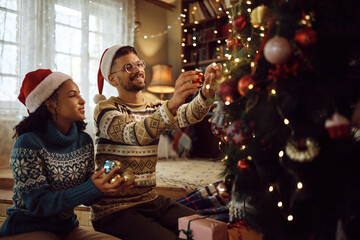 Obraz na płótnie Canvas Happy man and his black girlfriend decorating Christmas tree at home.