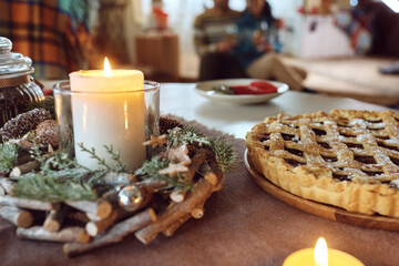Lit candle and Christmas pie on dining table with couple in background.