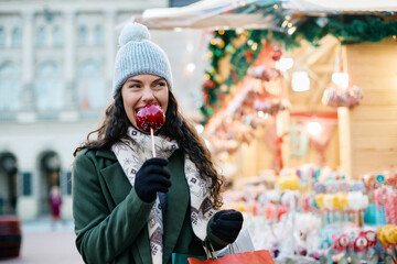 Happy woman eats candy apple at Christmas market.