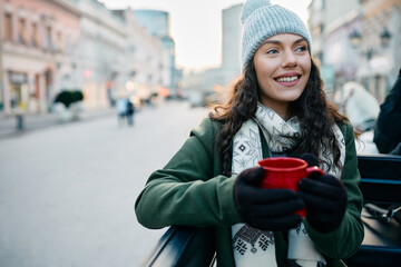 Smiling woman riding in carriages and drinking mulled wine during winter holidays.