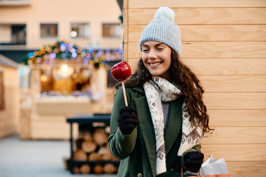 Young happy woman with taffy apple at winter fair during Christmas holidays.
