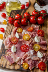 branch of ripe red cherry tomatoes on a cutting board and parma ham with buffalo mozzarella glass of oil and a glass of red wine