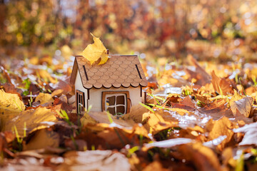 Wooden toy house in bright yellow autumn leaves. Concept image house. Concept of sale or purchase house, cozy ecological house