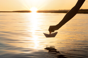 the paper boat goes on a big voyage at sunset, the boy's hand launches the origami ship on the water