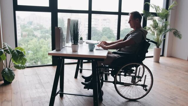 Disabled Businessman Sitting In Wheelchair Using Computer At Workplace