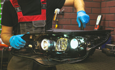 Car headlight in repair close-up. The car mechanic installs the lens in the headlight housing. The...