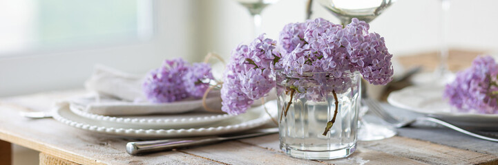 Beautiful table decor for a wedding dinner with a spring blooming lilac flowers. Celebration of a special event. Fancy white plates, and wineglasses. Countryside style. Banner