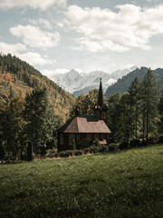 The wooden church of St. Anna in Tatranska Javorina - Slovakia with beautiful snowy mountains on background. Vertical landscape photo of wooden chapel under the hills with green grass suroundings.