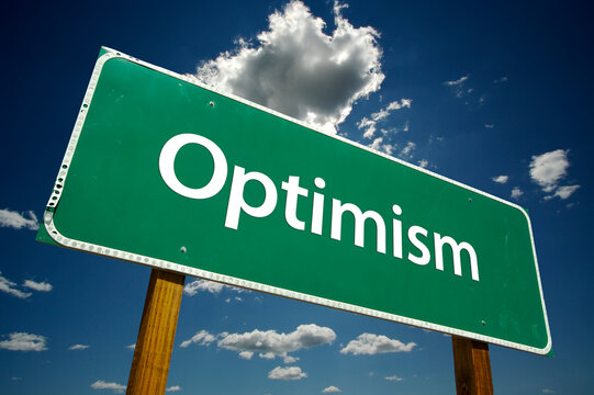 Optimism Green Road Sign On Cloudy Blue Sky Background