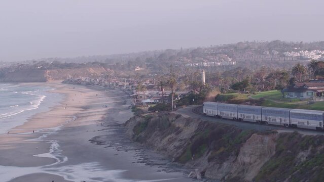 Aerial tracking train along coast of San Diego coastal bluffs and neighborhoods in California in purple sunset