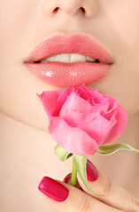 Close-up of young attractive women lips with beautiful roses. Attractive model girl's lips with makeup posing for beauty photoshoot. Closeup, selective focus.