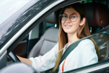 Portrait of young smiling woman driving new car, looking at the camera. Transportation, safety driving concept 