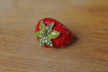 one red green strawberry shaped ring lies on a brown table