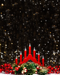 Christmas decorations view of red candle lights bridge, red berries and Christmas green round wreath colored in gold at the tips on dark background with silver and gold colors bokeh. Holidays advent