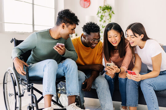 Group of diverse teenage people using mobile phone - Inclusion and diversity concept with young indian man in wheelchair having fun with multiracial friends watching social media content on cellphone