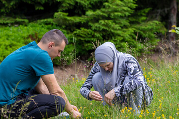 Young muslim couple picking blueberries in the forest. Boy and girl collecting organic wild bilberries, lifestyle and agricultural concept