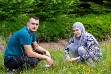 Young muslim couple squatting on grass and looking to the camera with different face expressions. Love, lifestyle and nature concept