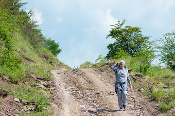 Young muslim girl wearing sport clothes walking alone on the rural mountain road. Woman with hijab showing hello by hand sign in the nature. Islam religion concept