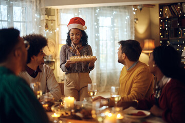 Happy black woman serving Christmas pie during dinner party with friends at home.
