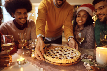 Close up of man serving sweet pie to his friends during Christmas meal at home.