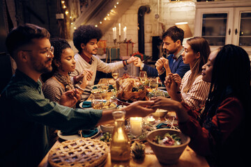 Multiracial group of friends saying grace during Thanksgiving dinner at dining table.