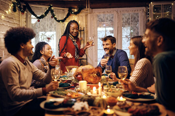Happy black woman holding toast during Thanksgiving meal with friends at dining table. - Powered by Adobe