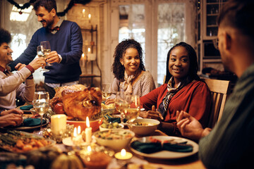 Happy black woman talks to friends during Thanksgiving meal at dining table.