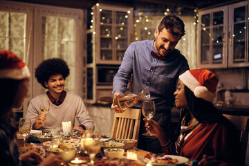 Happy man serving wine to his friends during Christmas dinner at dining table.
