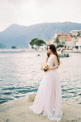 Fototapeta na wymiar Bride with a bouquet stands on the pier near the coast of Perast