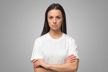European female standing with arms crossed showing doubt and mistrust on gray background