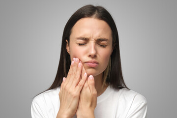 Miserable woman experiencing severe toothache, pressing palm to cheek, closing eyes because of pain - 538229249