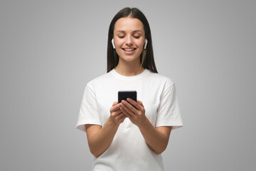 Fototapeta premium Pretty woman looking at smartphone, smiling on gray background