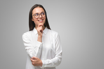 Business woman looking aside in spectacles dressed in formal clothes, on gray copy space background