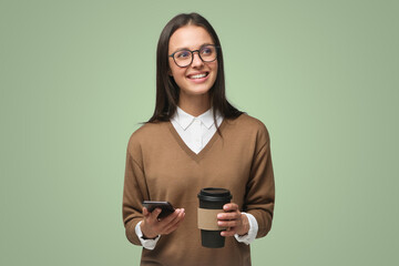 Portrait of beautiful young woman holding smartphone and takeaway coffee, isolated on green