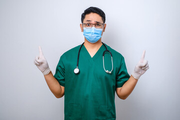 Surprised or curious male nurse in green scrubs, medical mask, pointing fingers up, inform patients how prevent corona infection