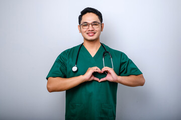 Lovely caring asian doctor male doctor in scrubs showing heart gesture and smiling