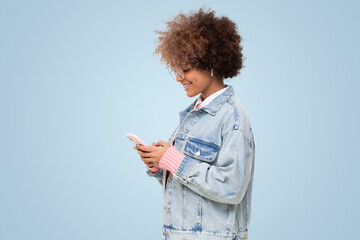 Side view of african american girl with afro hairstyle and glasses holding phone on blue background