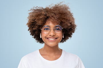 Portrait of smiling african student girl in white t-shirt and trendy glasses on blue background